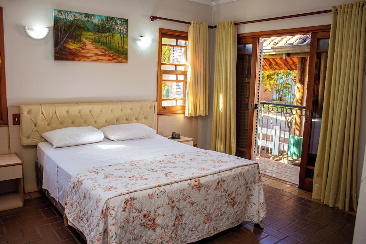 A bedroom with a large bed, a nightstand, a painting on the wall, and a view of the outside balcony.