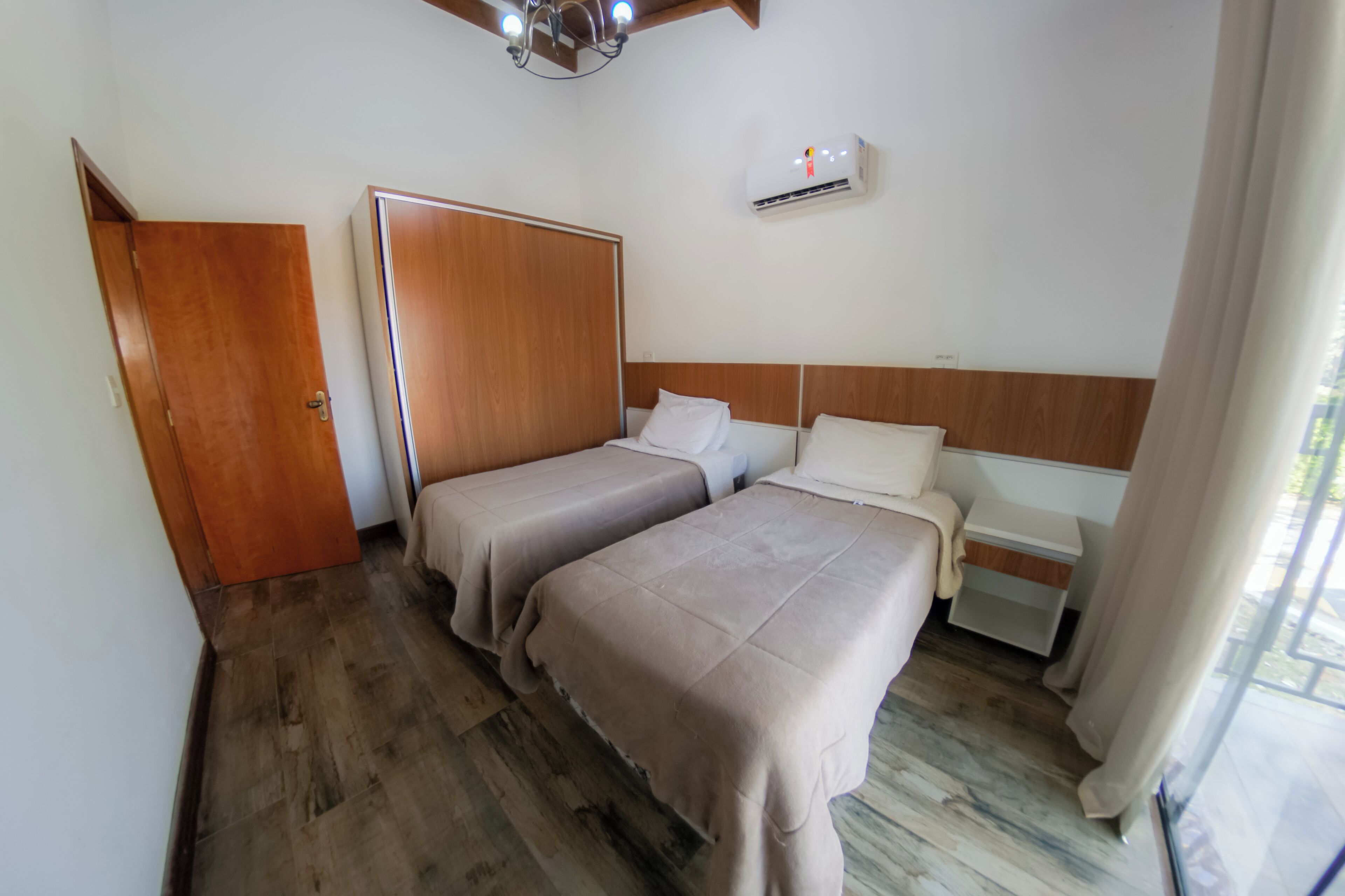 Ein Hotelzimmer mit zwei Betten, Holzboden, einem Kleiderschrank, einem Nachttisch und einer Klimaanlage.