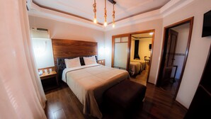 A bedroom with a wooden headboard, a large bed with a beige bedspread, a bedside table with a lamp, and a wooden floor. - Hotel Fazenda Pocos de Caldas (Poços de Caldas)