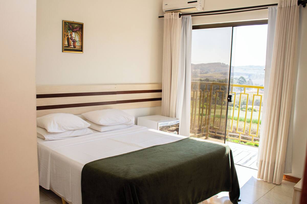 A hotel room with a bed, a nightstand, a painting on the wall, and a balcony with curtains.
