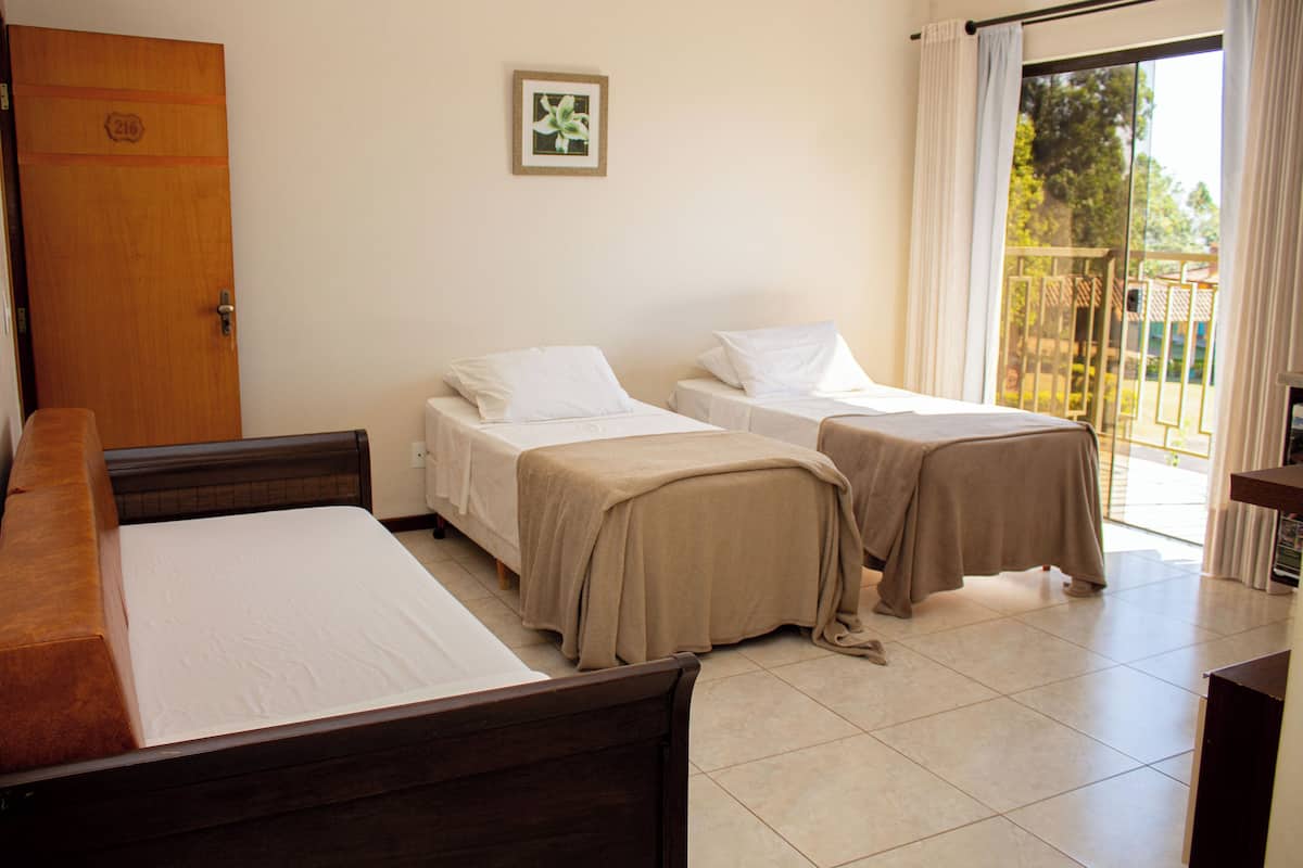 A hotel room with two single beds, a wooden desk, and a view of the outdoors through a sliding glass door.