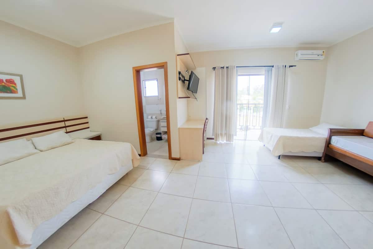 A hotel room with two beds, a TV, a bathroom, and a balcony with curtains.