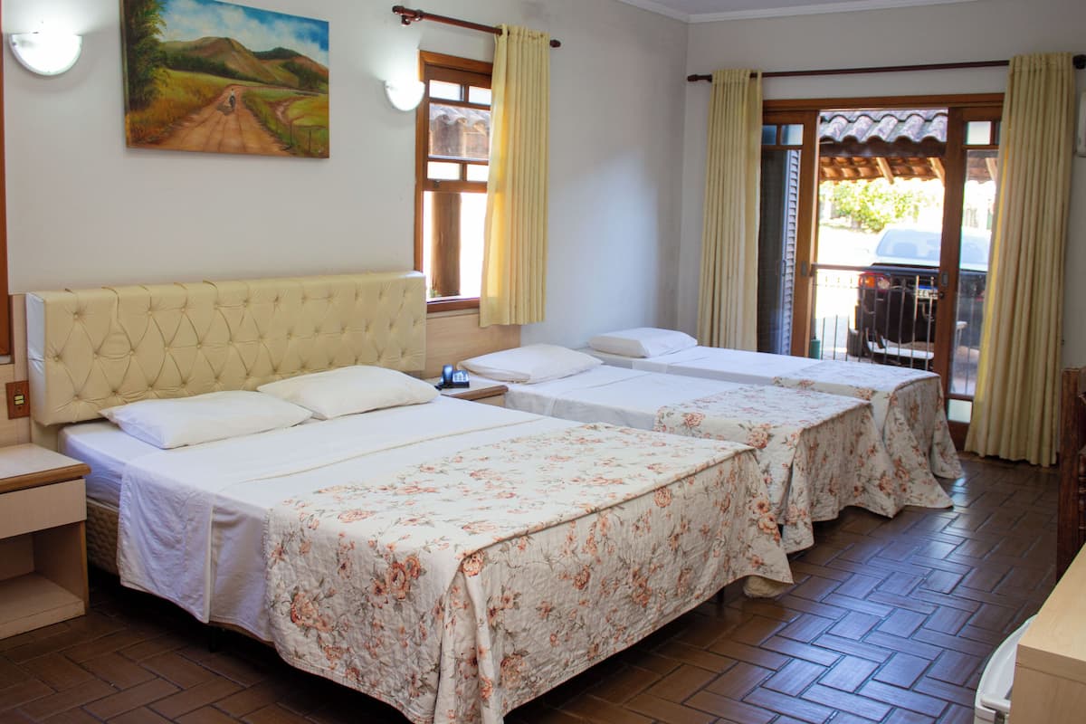 A hotel room with a large bed, two smaller beds, a wooden headboard, a painting on the wall, and a view of the outside through a door.