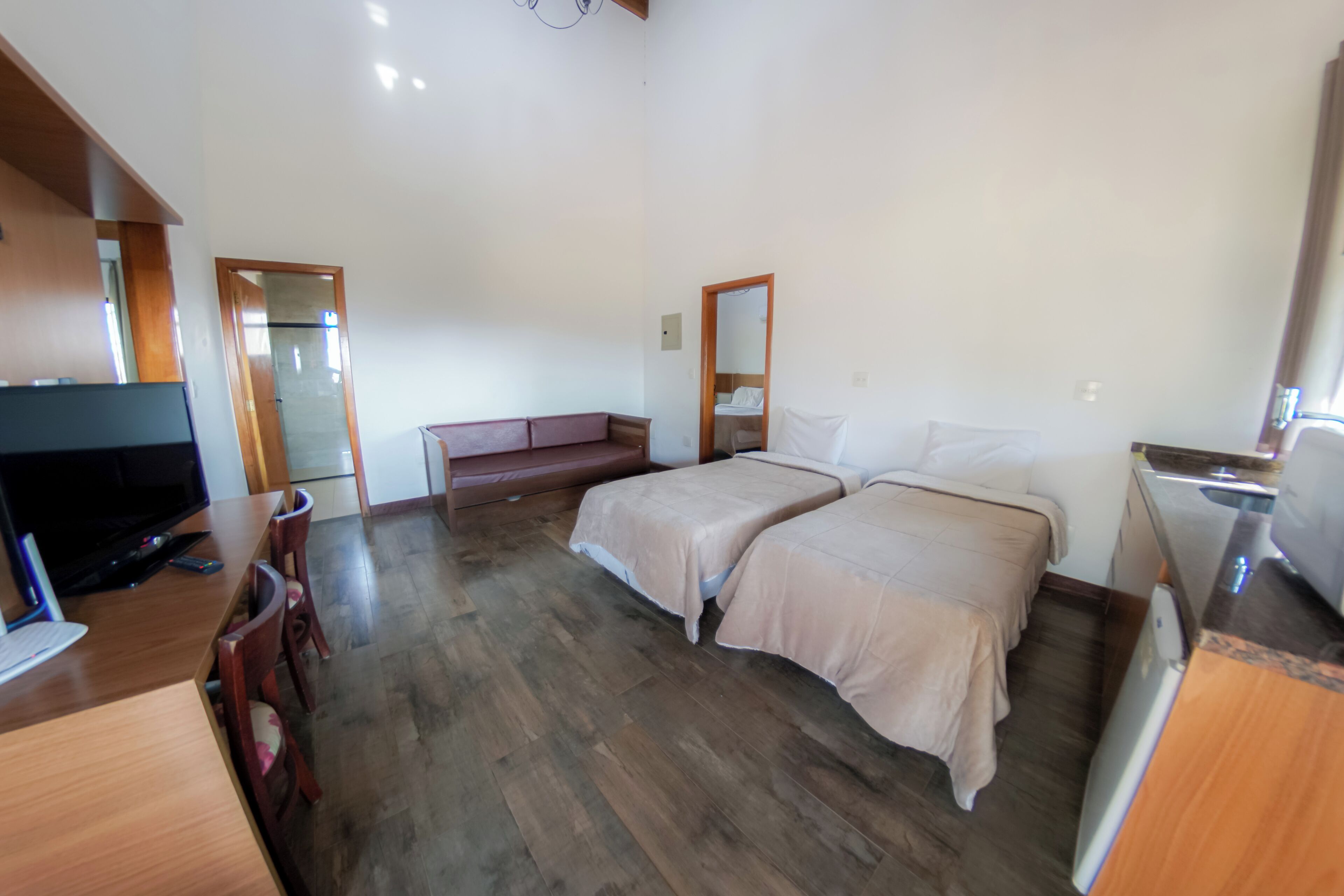 Una habitación de hotel con dos camas, un escritorio con televisor, piso de madera y un espejo.