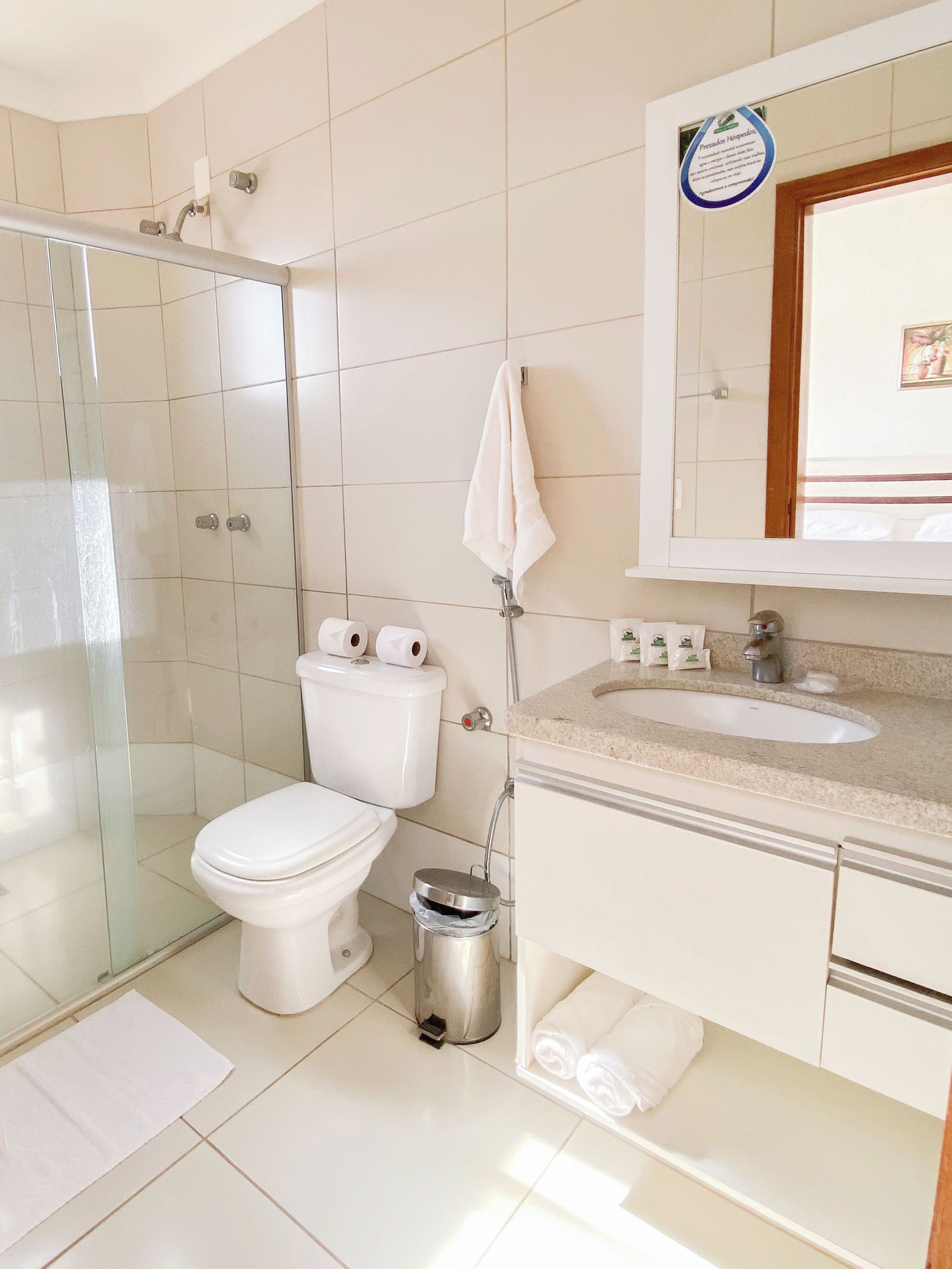 Un baño moderno con cabina de ducha de vidrio, inodoro, lavamanos con tocador y cubo de basura.