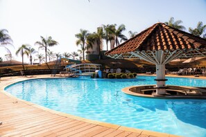 A swimming pool with a wooden deck, a water fountain, and a palm tree-lined background. - Hotel Fazenda Pocos de Caldas (Poços de Caldas)