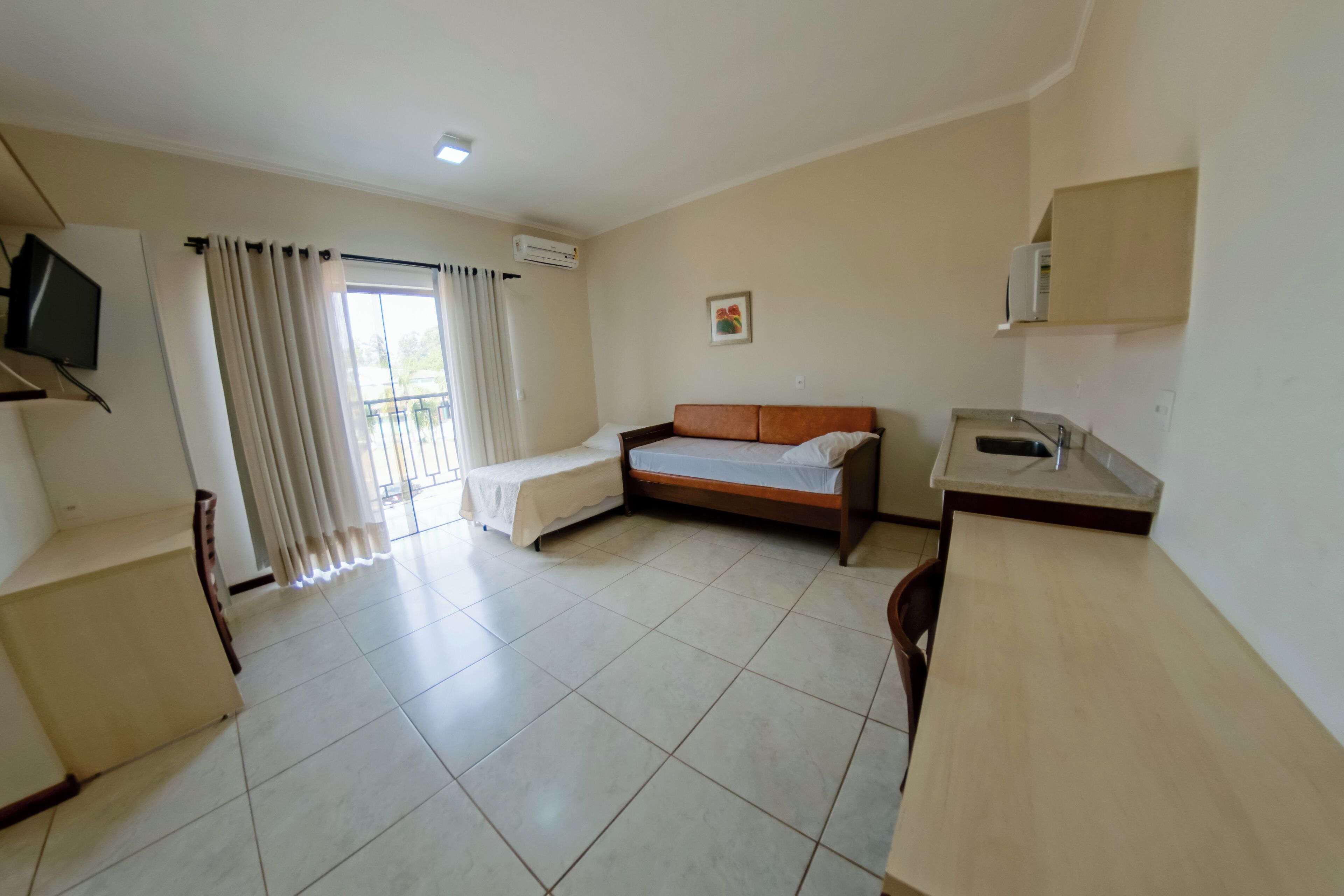 A hotel room with a bed, a small desk, a TV, and a window with curtains.