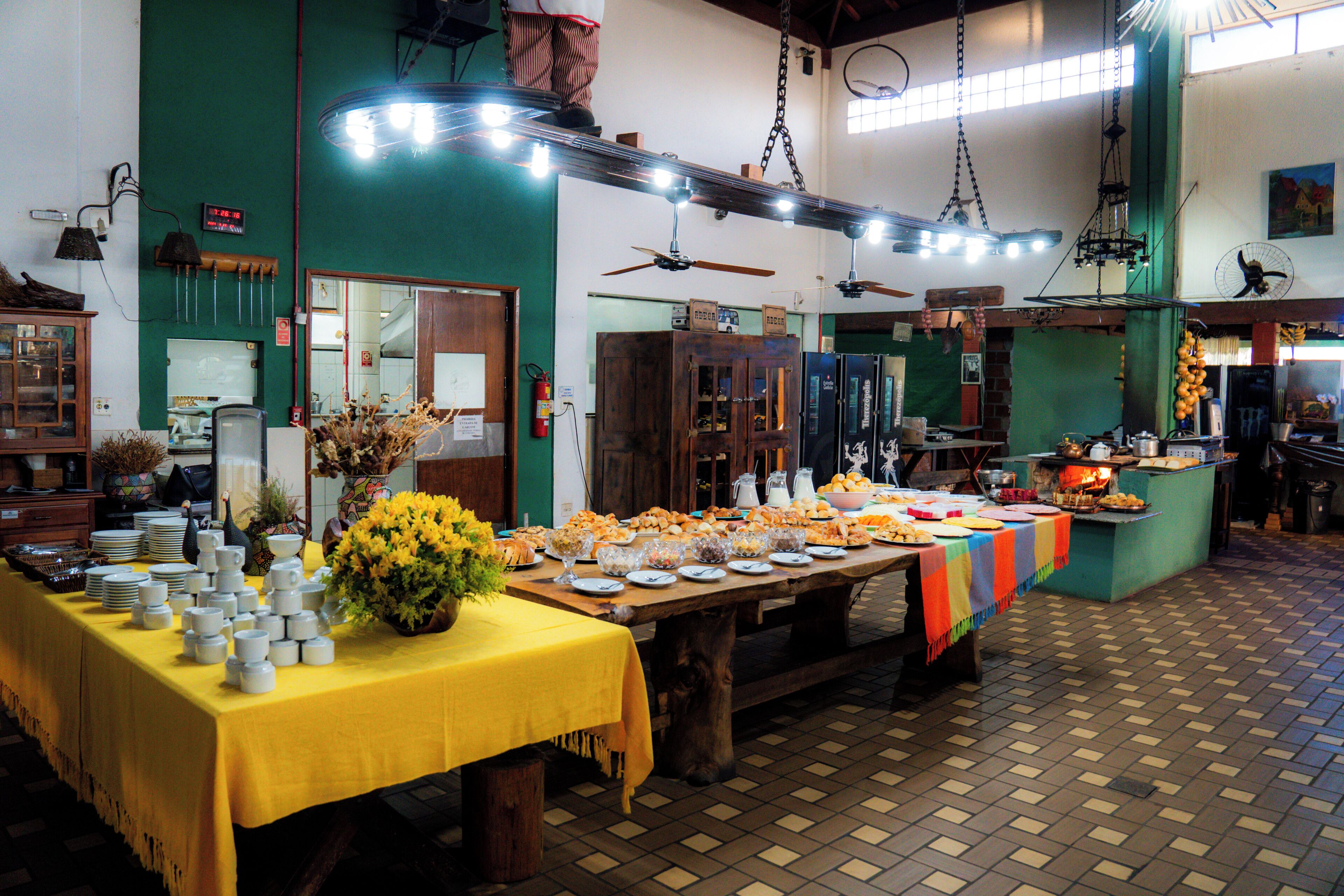 A buffet setup with multiple tables covered in yellow tablecloths, various food items, and a large floral centerpiece.