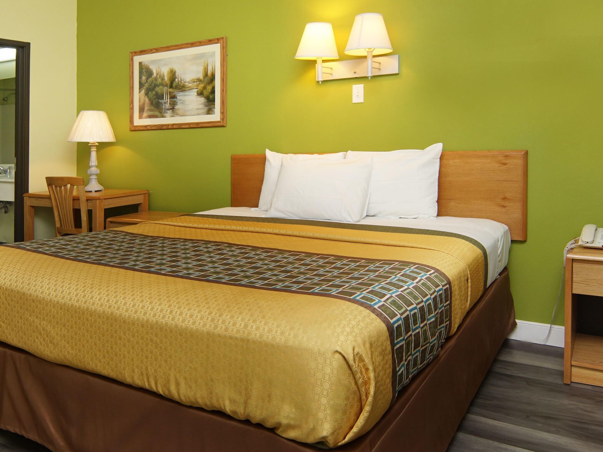 Camera d'albergo con un letto grande, una testiera in legno, due lampade ai comodini, un quadro incorniciato, un tavolino con una lampada e un telefono su un comodino.