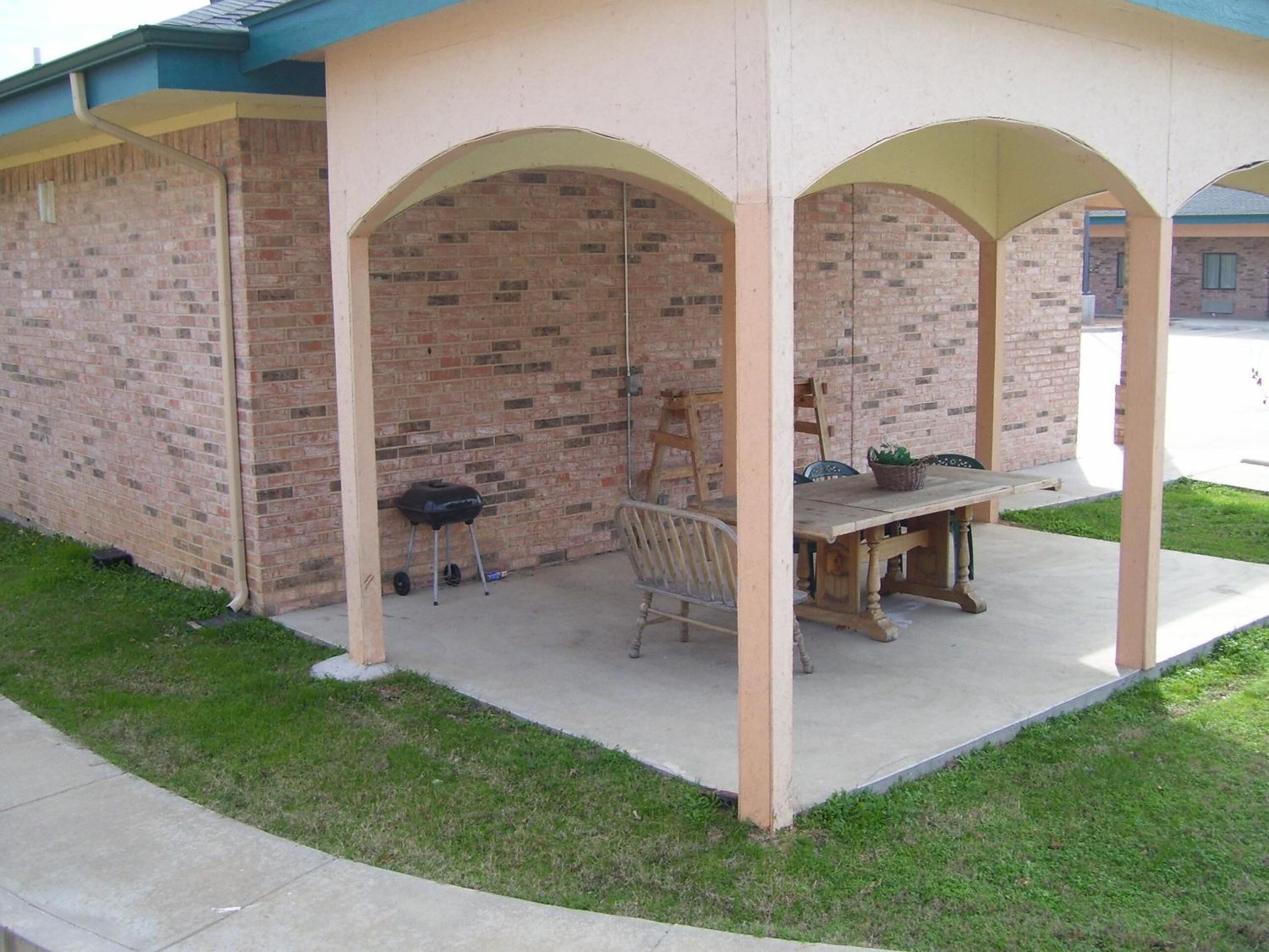 Un patio couvert avec un mur en briques, une table en bois et une chaise.