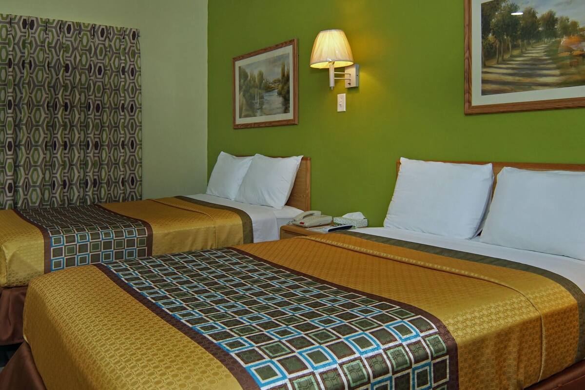 A hotel room with two beds, green walls, patterned curtains, and a painting.