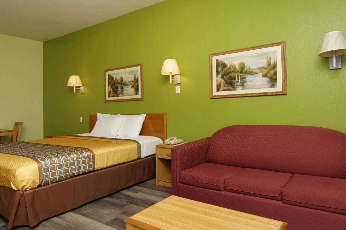 A hotel room with a bed, a red sofa, a wooden table, and two wall-mounted lamps.