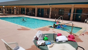 A pool area with lounge chairs and umbrellas, a brick building with green doors, and a clear sky. - Quality One Motel (Weatherford)