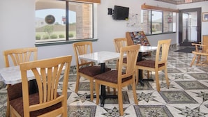 A dining area with wooden chairs and tables, a tiled floor, and a window with a view of the outside. - Quality One Motel (Weatherford)