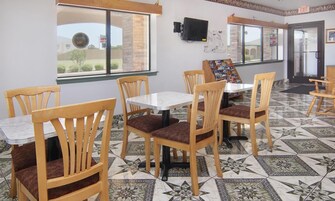 Un comedor con sillas y mesas de madera, piso de baldosas y una ventana con vistas al exterior.