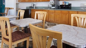 A small kitchen with wooden cabinets, a coffee machine, and a dining area with wooden chairs and a marble table. - Quality One Motel (Weatherford)