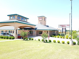 Un motel con un letrero que dice "Quality One Motel", con fachada de ladrillo, un área de estacionamiento techada y setos bien recortados.