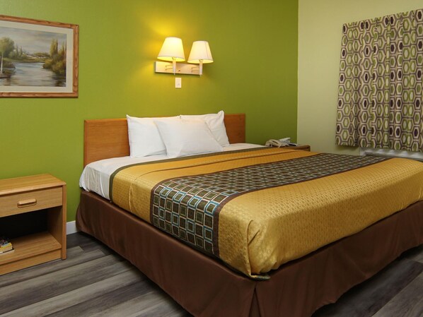 A hotel room with a bed, bedside table, lamp, and a painting on the wall.
