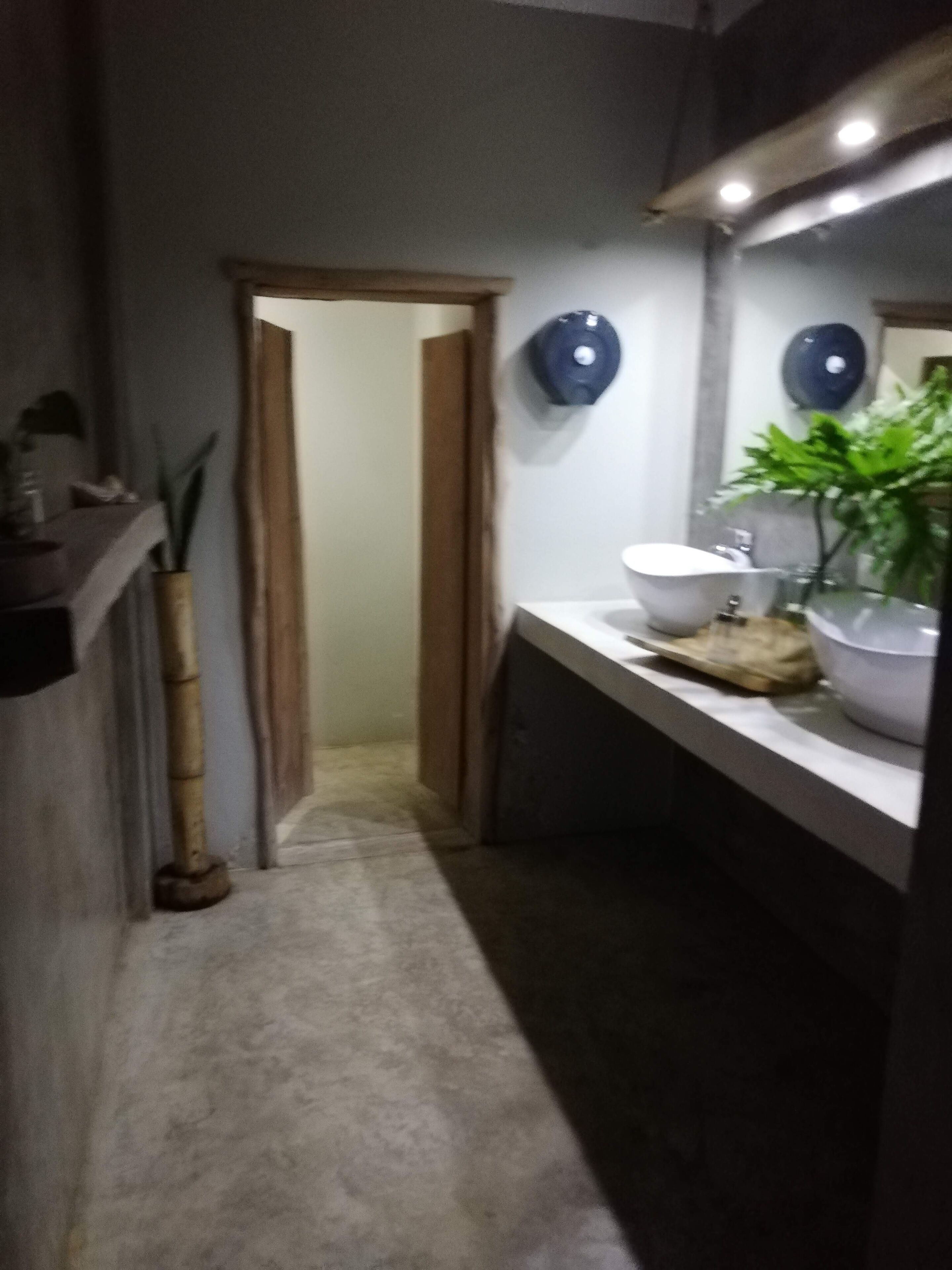 A narrow hallway with a wooden door at the end, a white sink, and a mirror on the wall.