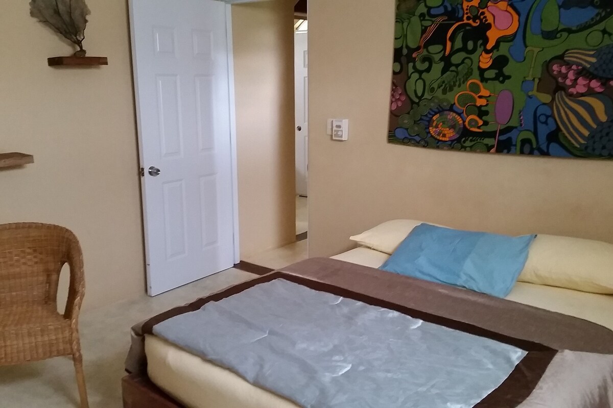 Une chambre à coucher avec un lit, une chaise, une porte et une décoration murale colorée.
