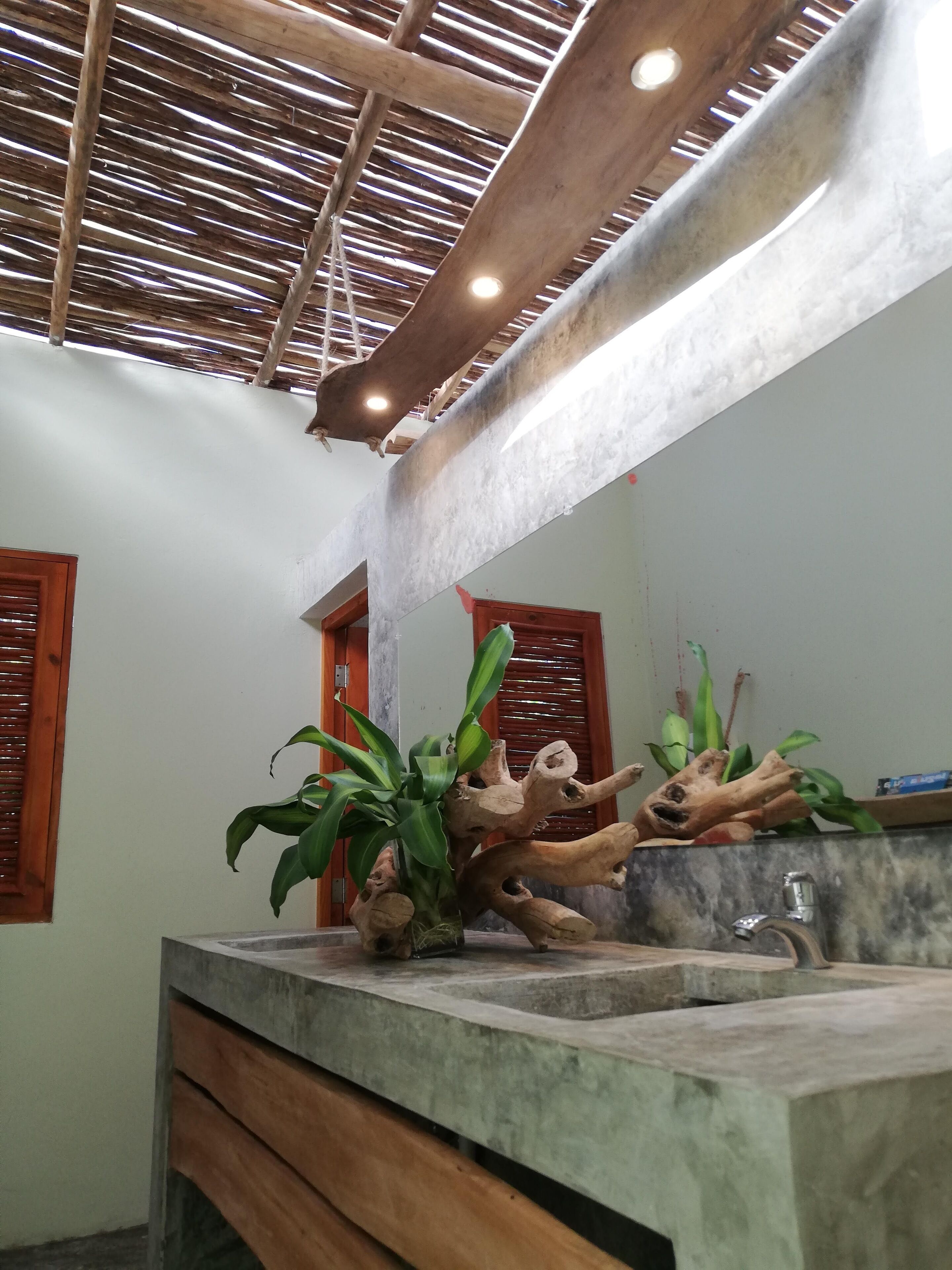Un baño con techo de madera, lavamanos de mármol y arreglos de plantas.