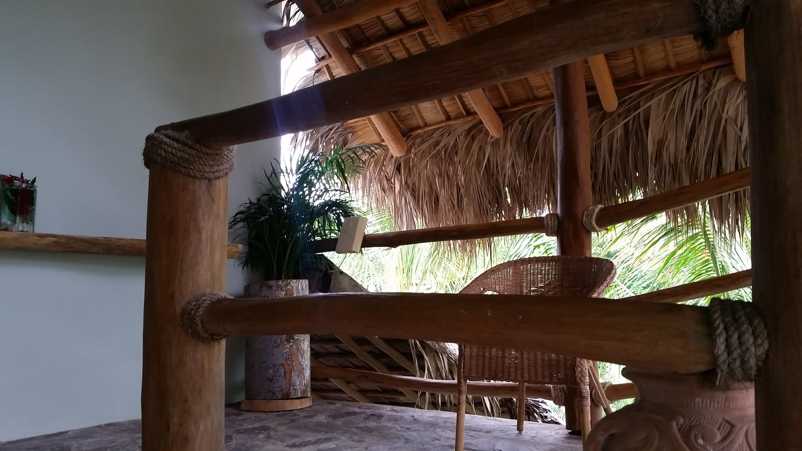 A rustic wooden structure with a thatched roof, a wicker chair, and a potted plant.