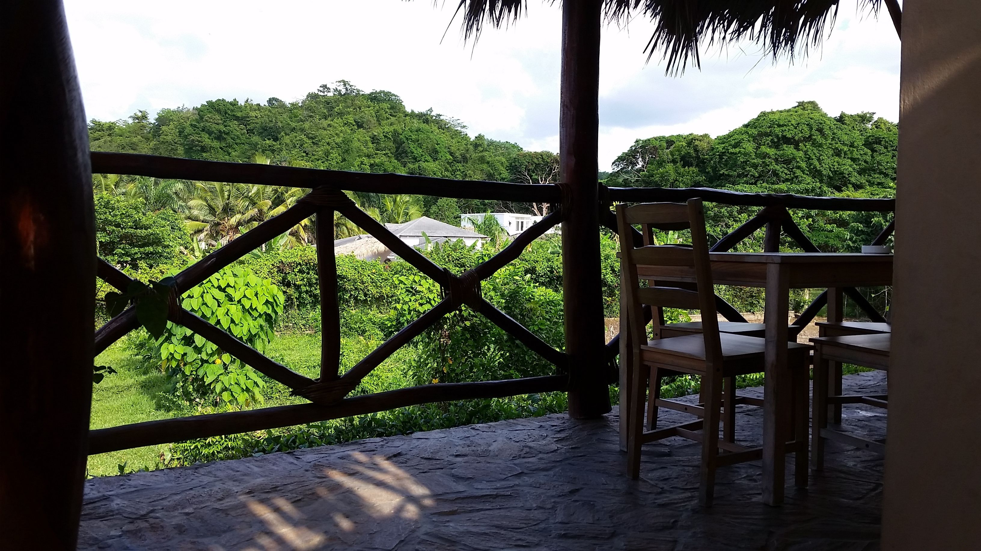A wooden chair and table on a stone deck with a view of lush greenery and trees.