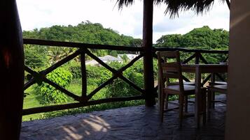 A wooden chair and table on a stone deck with a view of lush greenery and trees.