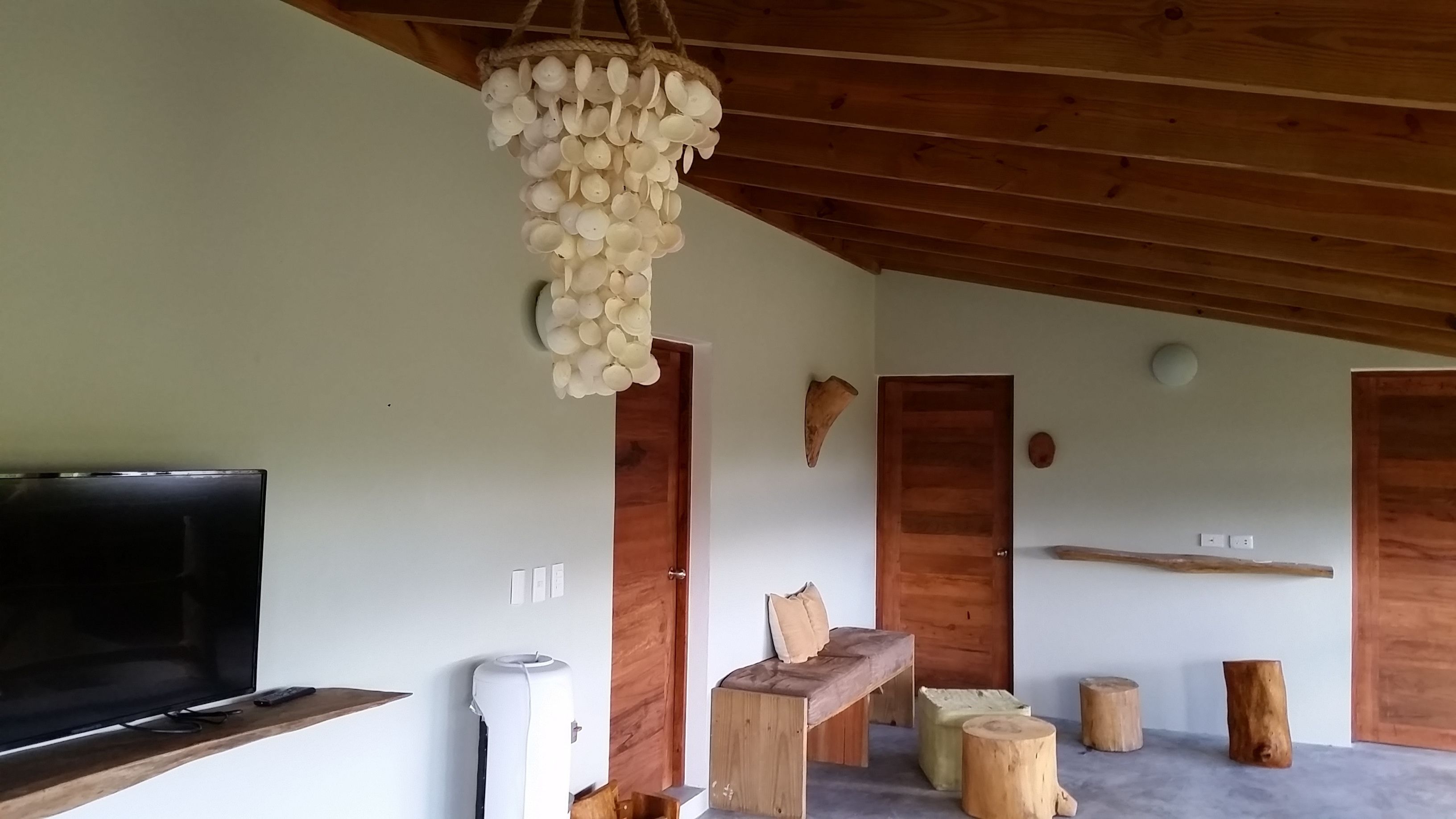 A room with a wooden ceiling, a television on a wooden shelf, a white air purifier, and a wooden bench.