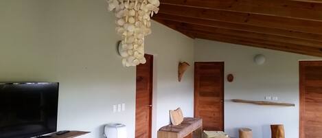 A room with a wooden ceiling, a television on a wooden shelf, a white air purifier, and a wooden bench.