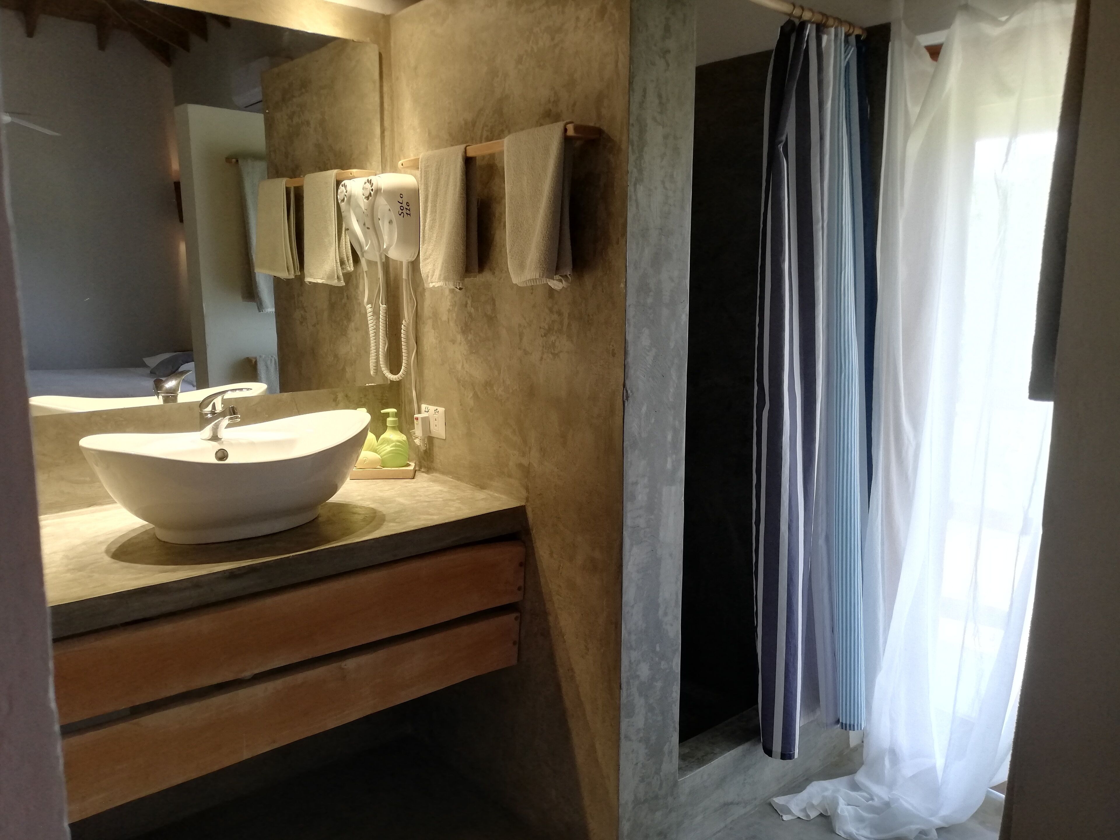 Une salle de bain avec un grand lavabo blanc, un meuble-lavabo en bois, un porte-serviettes et un rideau de douche.