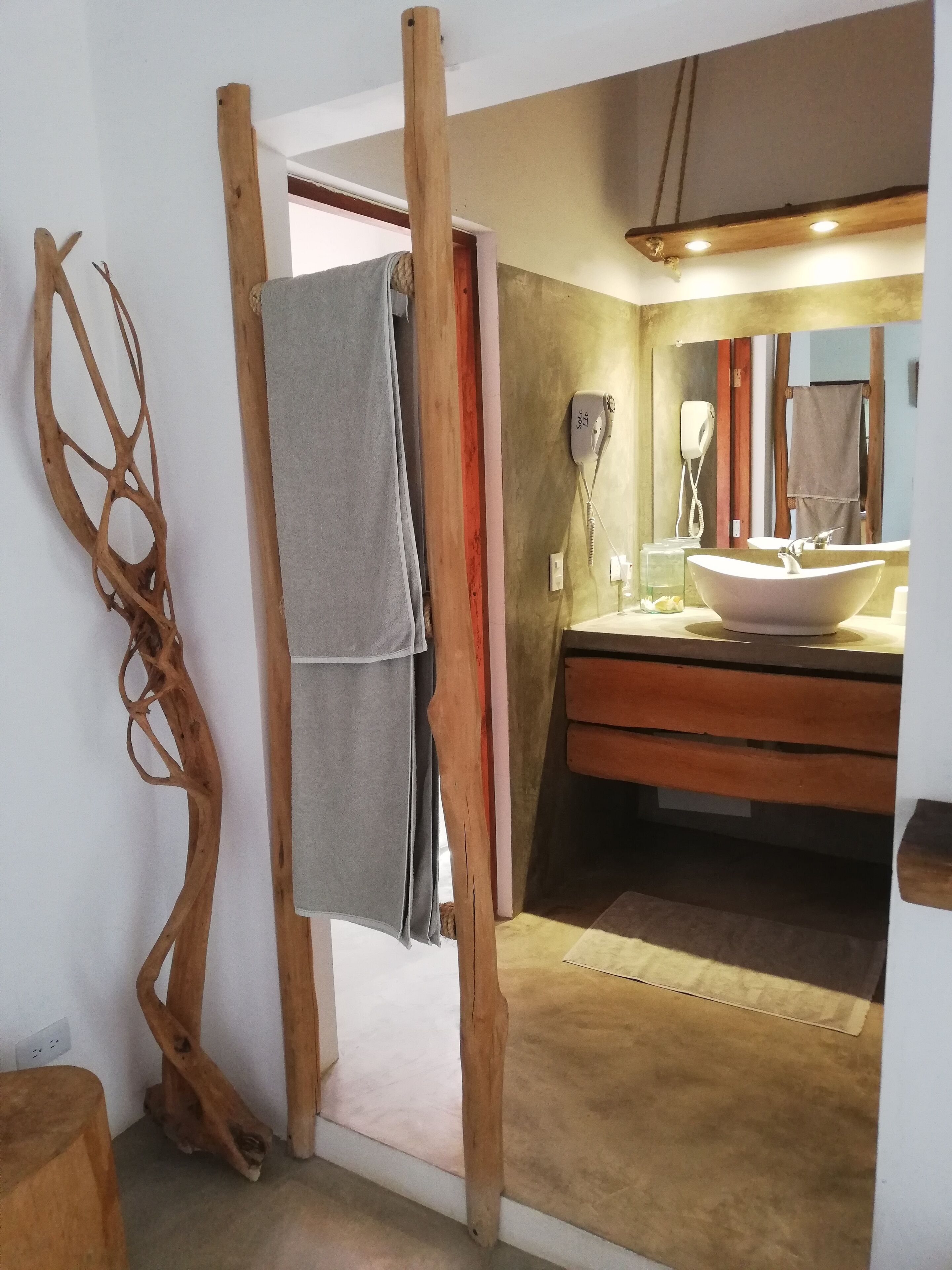 A bathroom with a wooden towel rack, a towel hanging, a hairdryer, and a sink with a mirror above it.