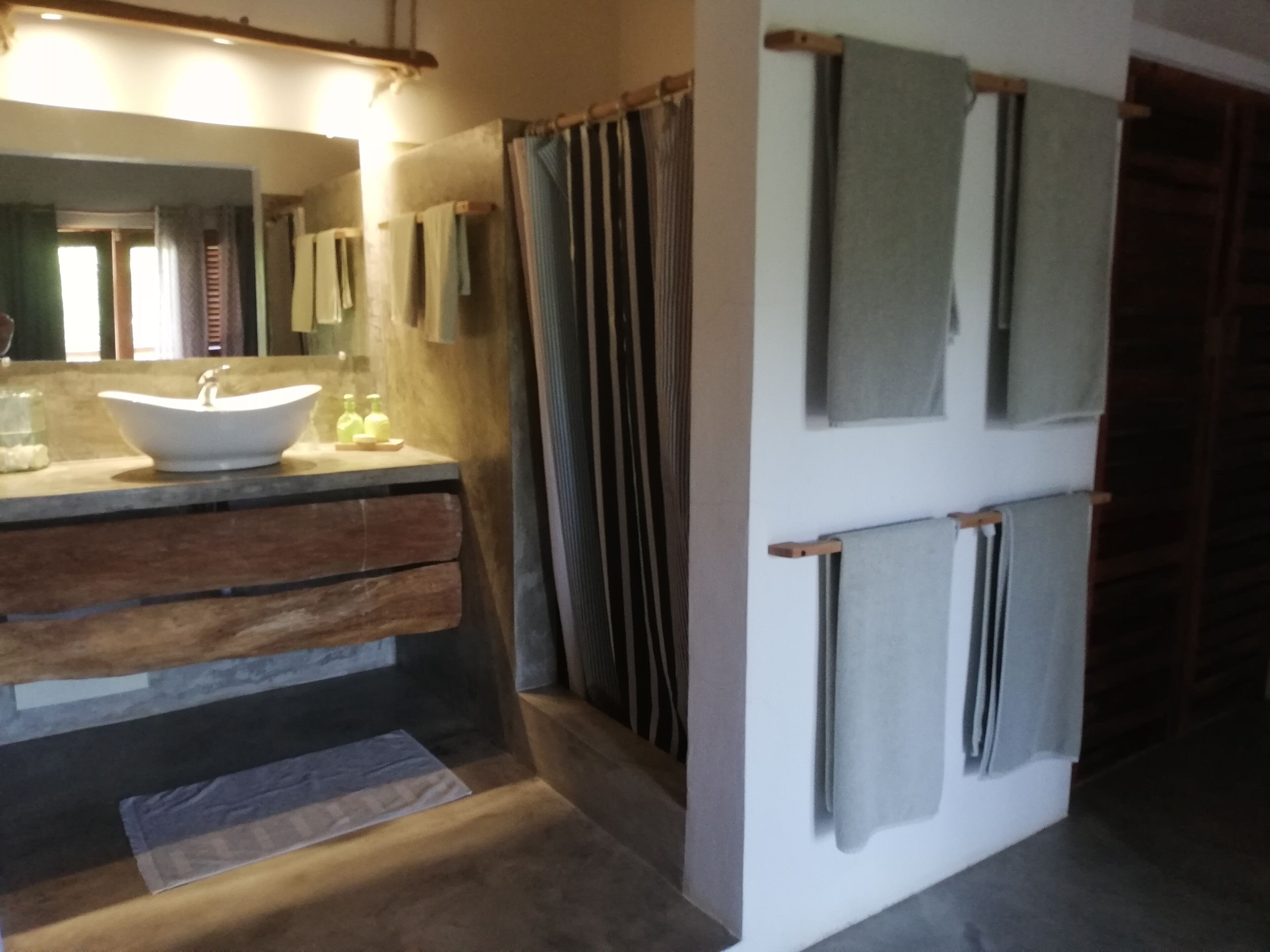 A bathroom with a wooden vanity, a large mirror, and multiple towels hanging on a rack.