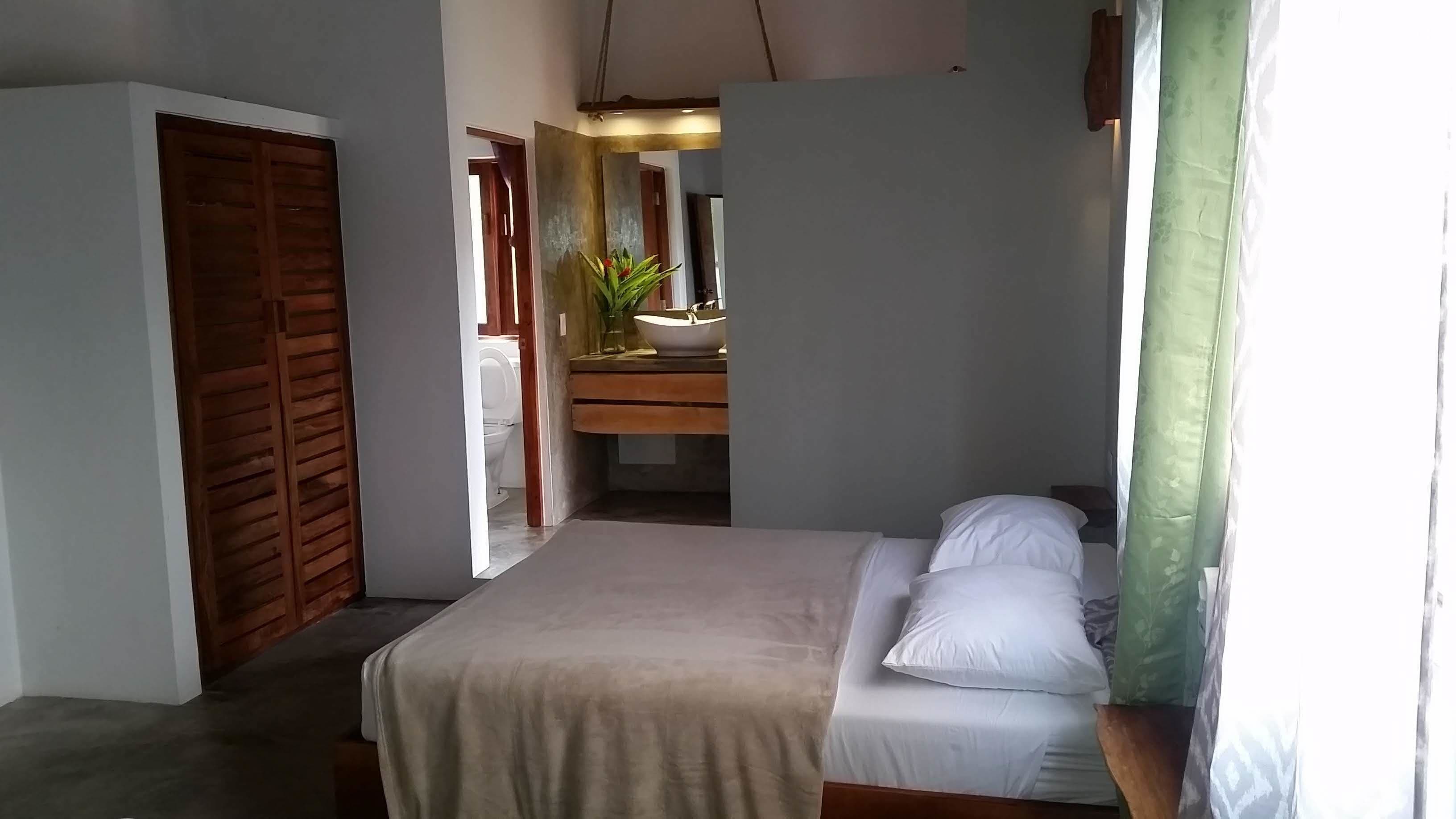 Un dormitorio con cama, armario de madera, baño con lavabo y espejo, y cortina verde.