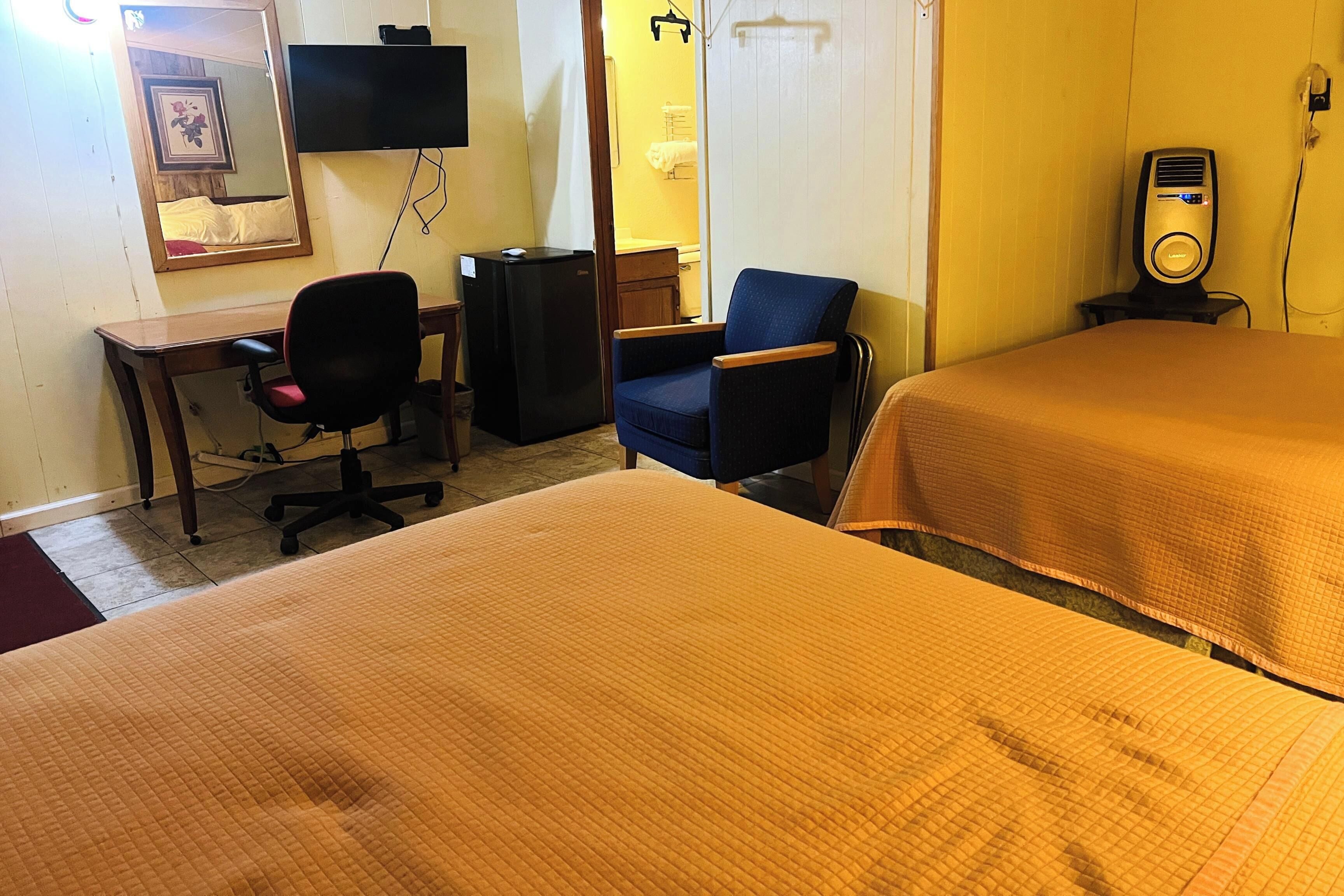 Een hotelkamer met twee bedden, een bureau, een stoel, een televisie, een verwarming en een spiegel.