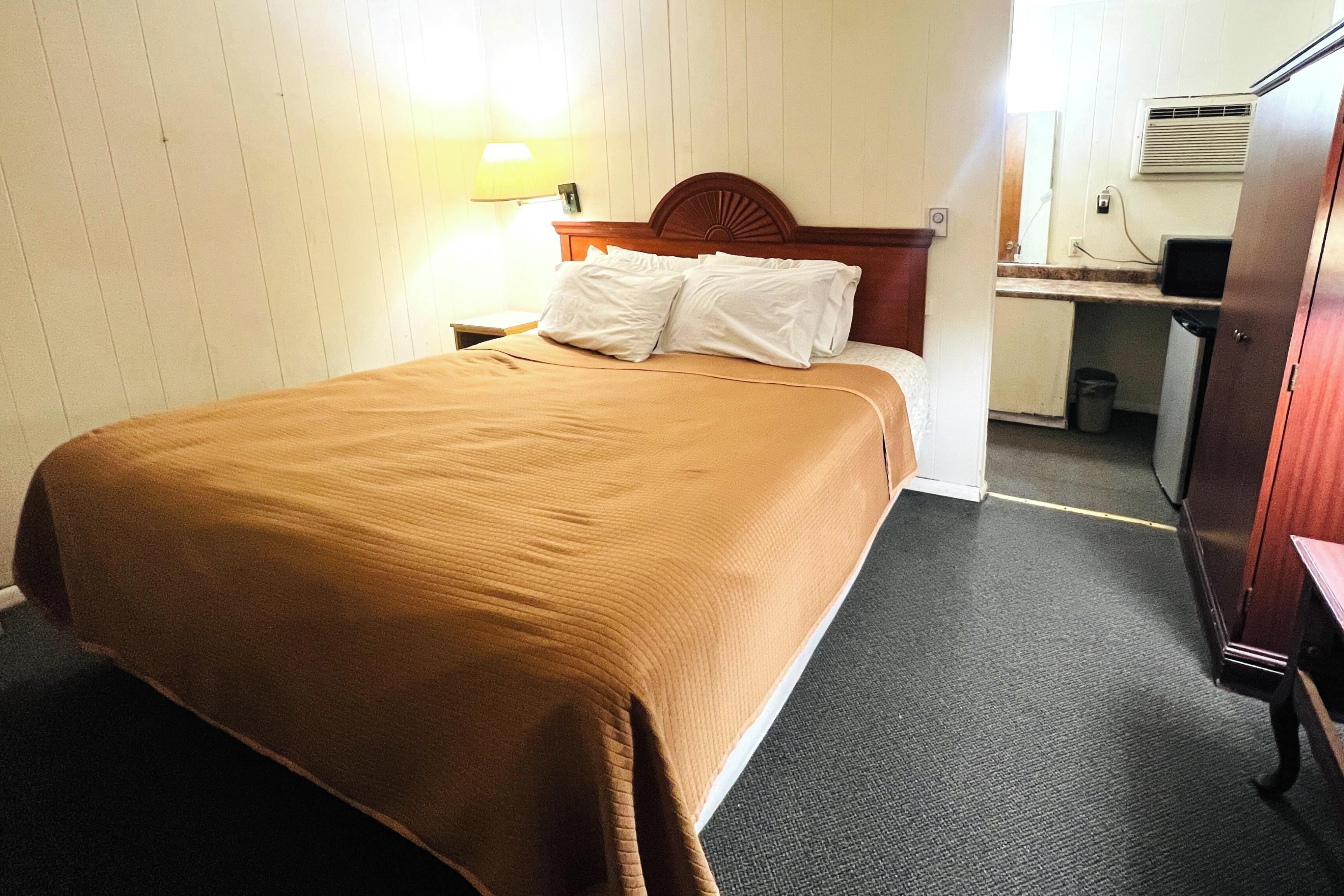 Una camera d'albergo con un letto, un comodino, una scrivania con una sedia, un cestino e un armadio.