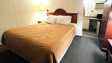 Una camera d'albergo con un letto, un comodino, una scrivania con una sedia, un cestino e un armadio.