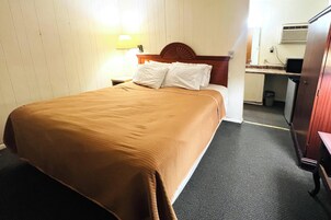 Habitación de hotel con una cama, una mesita de noche, un escritorio con una silla, un cubo de basura y un armario.