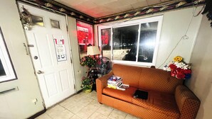 A room with a sofa, a fan, a door with a sign, and a window. - Sparta Motel Near St. Louis / Mississippi River IL (Sparta)