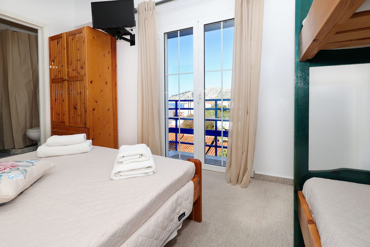 A room with a bed, a wooden wardrobe, and a balcony with a blue railing.