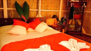 Un lit bien fait, avec une literie rouge et blanche, une tête de lit en bois et une table de chevet sur laquelle se trouvent une lampe et une petite plante.