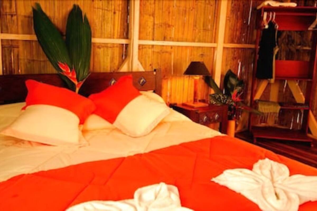 Ein ordentlich bezogenes Bett mit roter und weißer Bettwäsche, ein Holz-Kopfschild und ein Nachttisch mit einer Lampe und einer kleinen Pflanze.