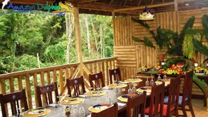 Un espace repas avec des tables et des chaises en bois, entouré d’une terrasse en bois offrant une vue sur une végétation luxuriante.