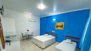 Una habitación de hotel con dos camas, una mesita con sillas, un cuadro en la pared y un equipo de aire acondicionado.