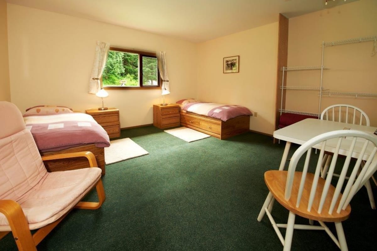 A cozy bedroom with two beds, a chair, a table, and a window with curtains.
