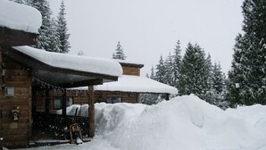 A wooden cabin with a snow-covered roof and a large snowbank in front. - Shames Country Lodge (Terrace)