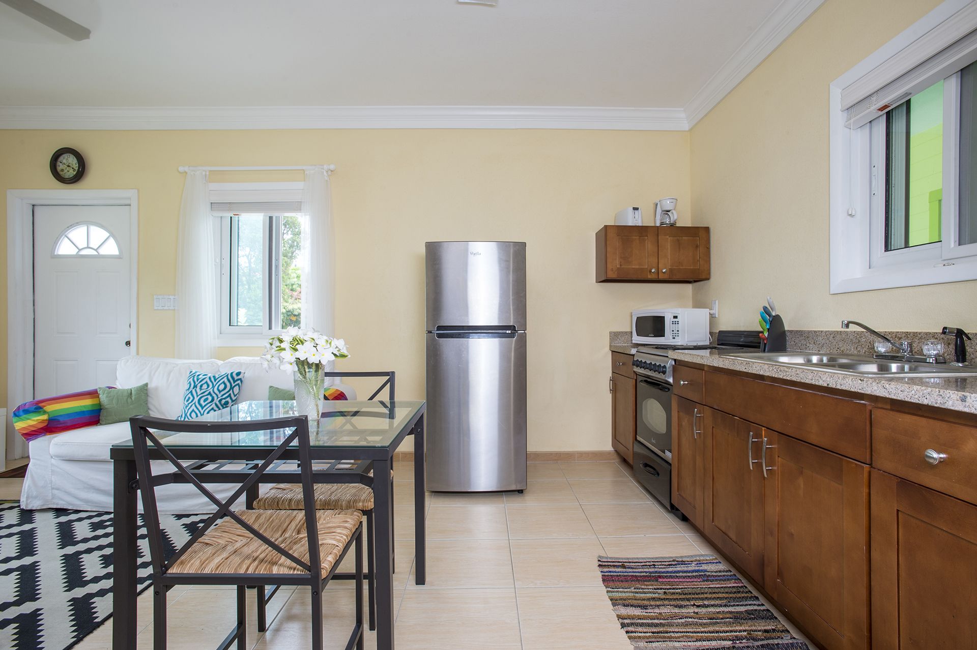 A modern kitchen with a stainless steel refrigerator, microwave, and oven. There is a dining area with a glass table and chairs, and a kitchen counter with a sink.