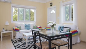 Un salón luminoso con una mesa de comedor de cristal, sofás blancos con cojines de colores, una mesita auxiliar blanca y una silla negra de fibra.