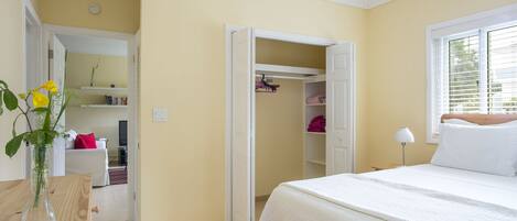 Une chambre à coucher avec un lit, une table de chevet et une commode. On y trouve un placard avec des vêtements suspendus et une étagère avec des livres.