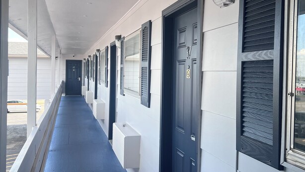 A long corridor with a blue floor, white walls, and black doors with shutters. - Regency Inn and Suites (Dodge City)